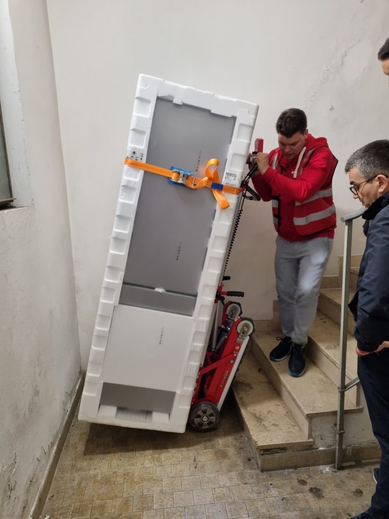 A man carries a household appliance down the stairs with the electric stair climbing trolley Buddy Lift.